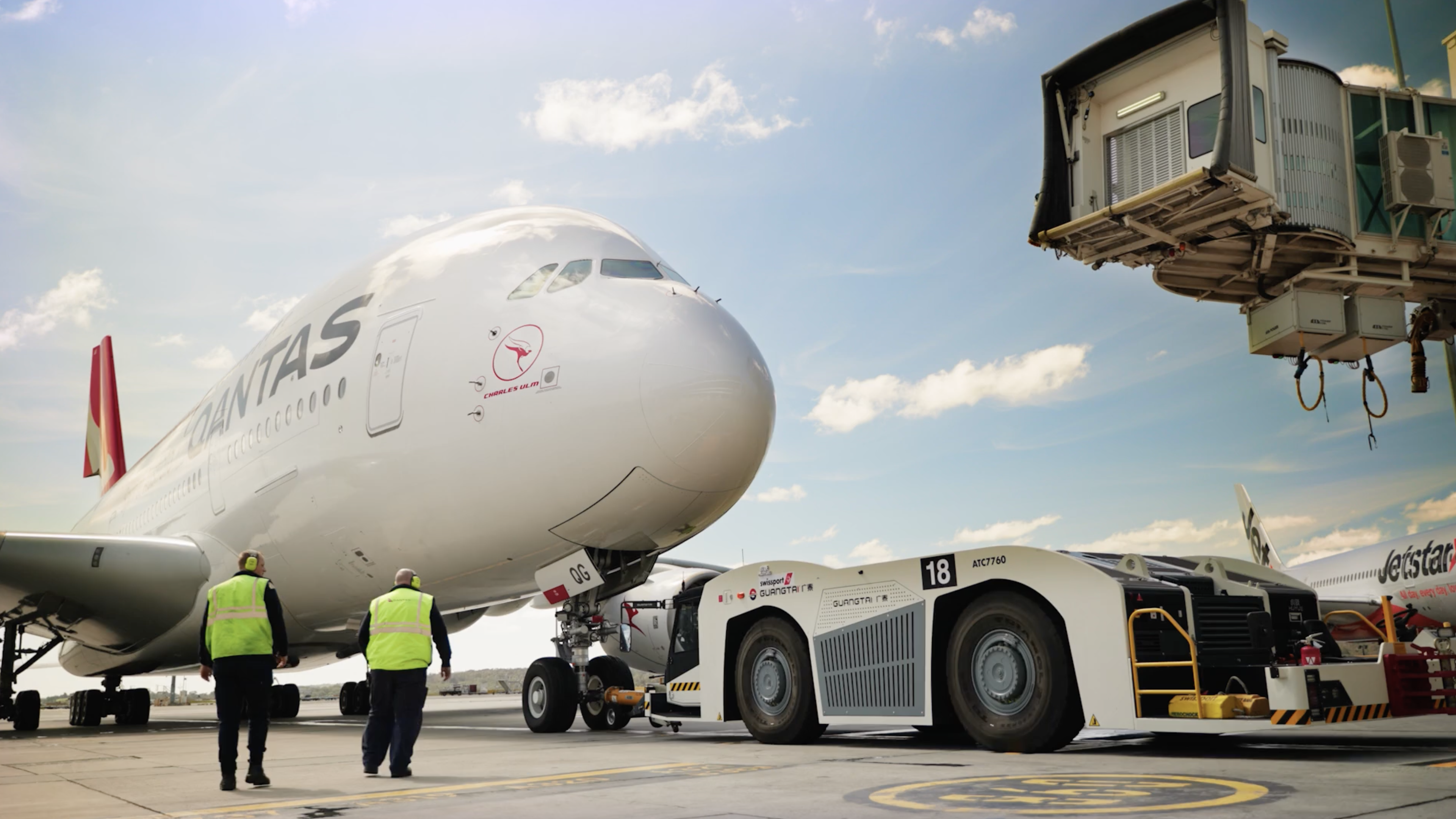 An airplane is parked at the airport with employees nearby and a ground vehicle.