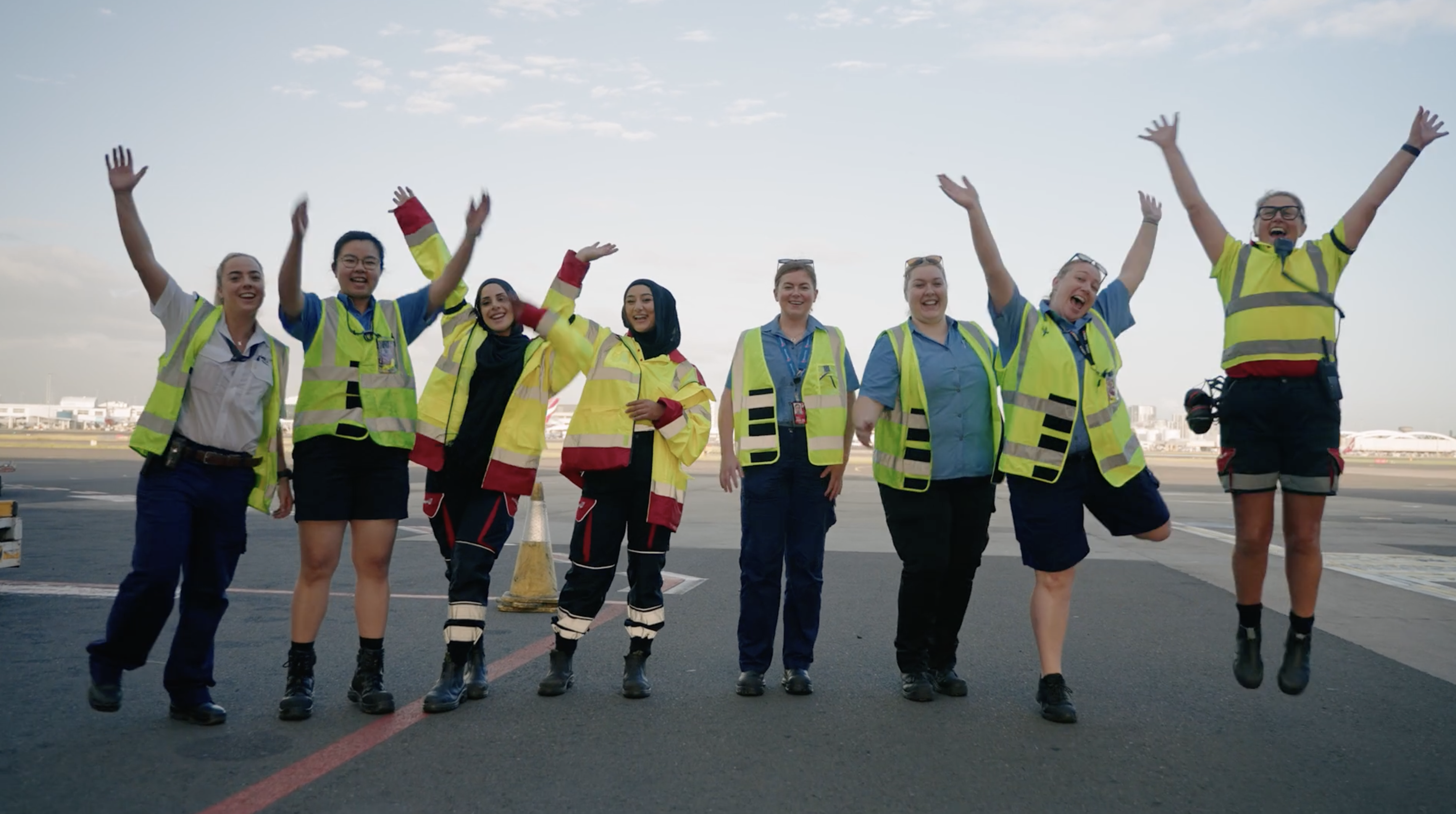 Group of airport workers in safety vests joyfully waving on the tarmac.